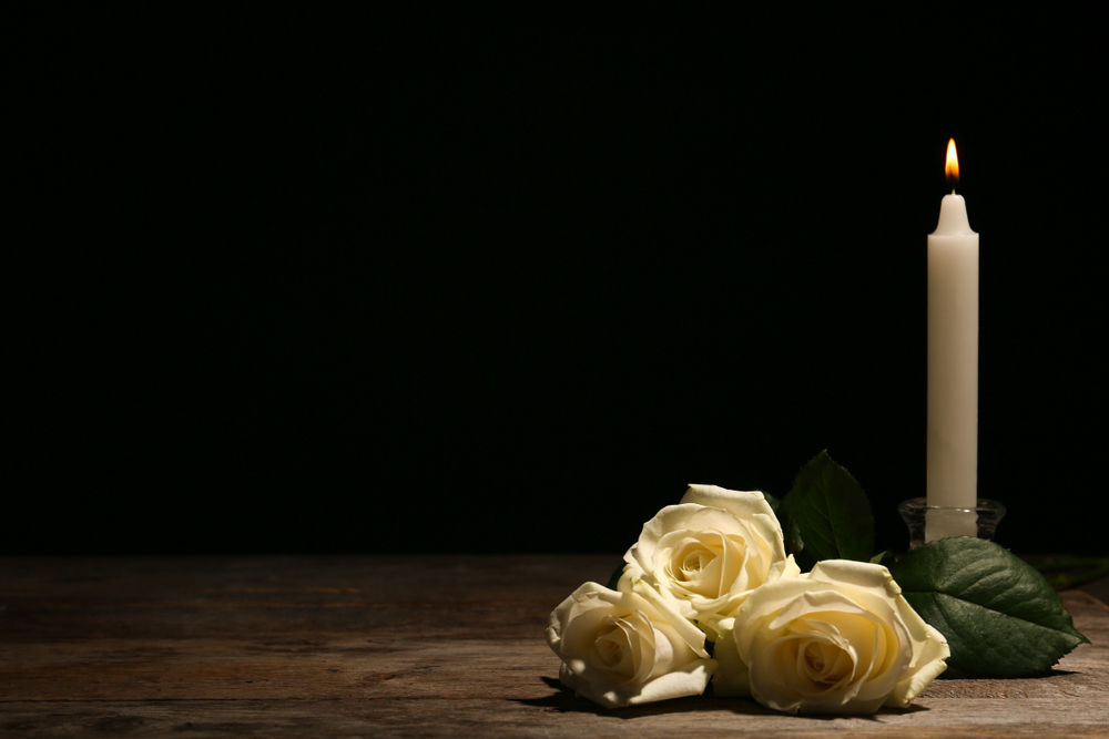 Eine Kerze und Blumen vor dunklem Hintergrund.